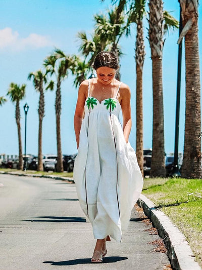 Femme portant une robe blanche d’été avec imprimé palmier, marchant dehors en plein soleil.