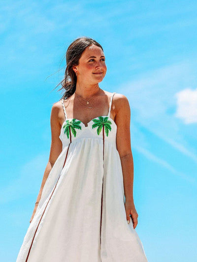 Vue de profil d’une femme portant une robe blanche à palmiers sous un ciel bleu.