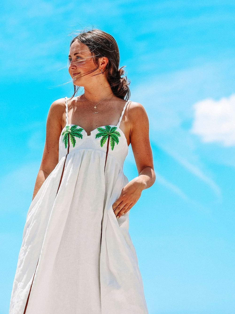  Vue de profil d’une femme portant une robe blanche à palmiers sous un ciel bleu.